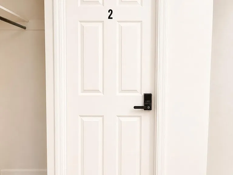 Interior hallway with wood-look flooring, clean white trim, and a numbered door with keyless entry lock.