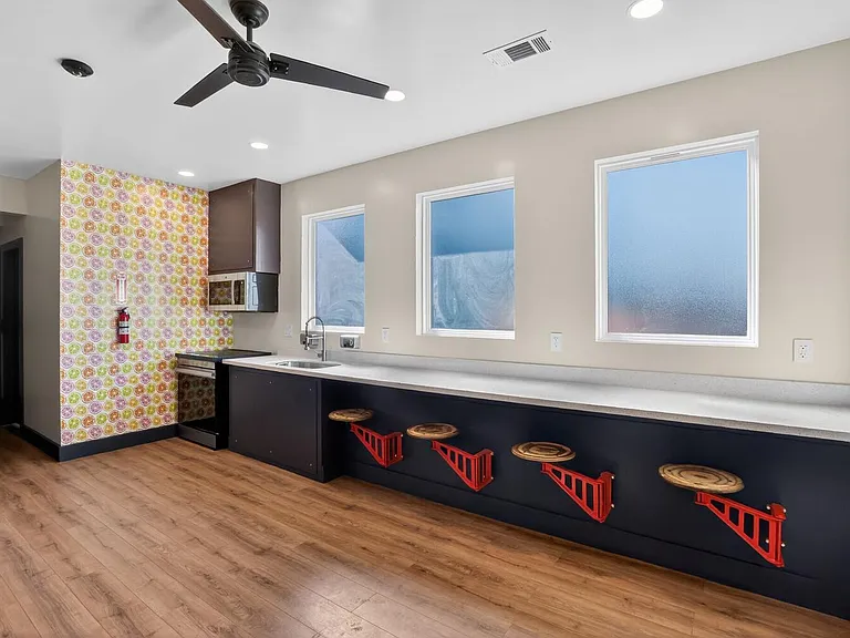 Kitchen space with long breakfast bar seating, microwave and sink, plus multiple windows and recessed lighting.