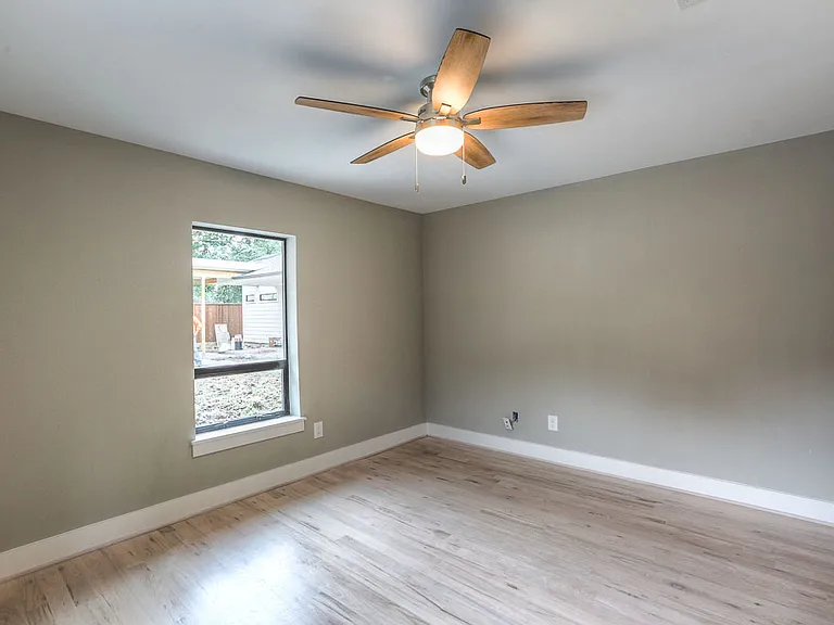 Quiet rear bedroom with hardwood floors, ceiling fan, and a picture window with backyard view