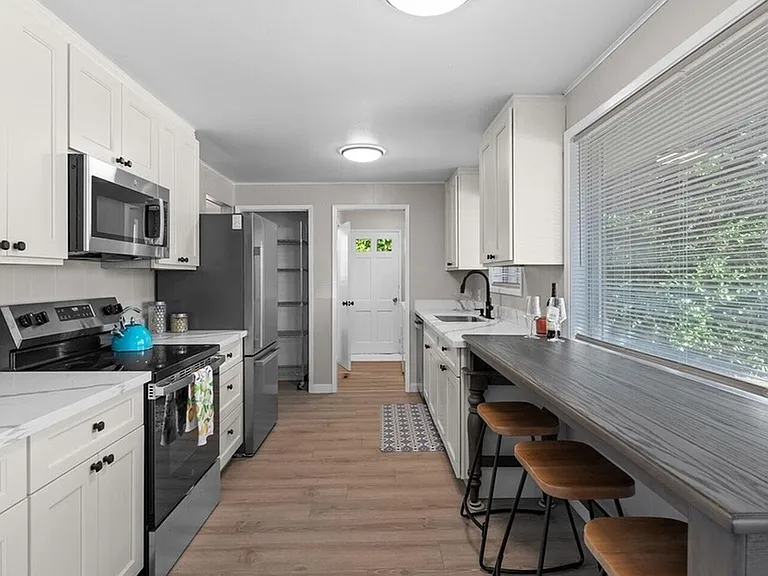 Galley kitchen with ample counter space, stainless appliances, pantry storage, and a window-side breakfast bar.