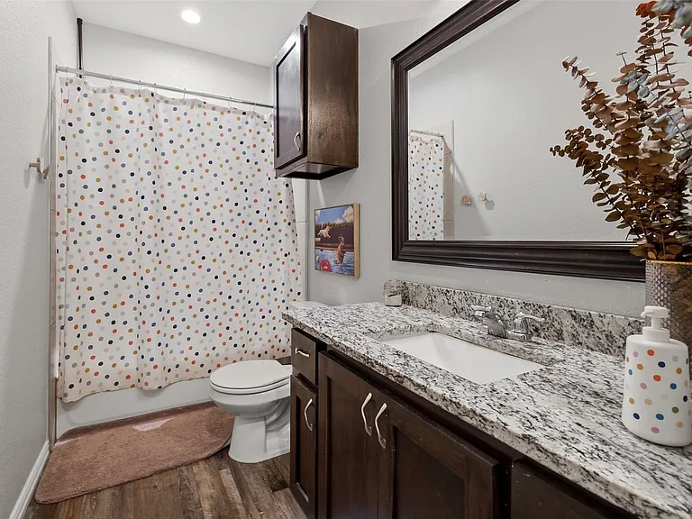 Bathroom featuring a white porcelain toilet, wood-finish flooring, a vanity with a white countertop, an undermount sink, and a framed mirror