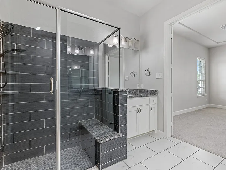 Spa-inspired ensuite bath featuring dual granite vanities, a framed walk-in shower with bench seating