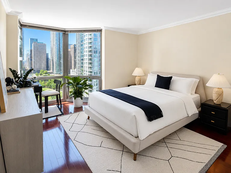 Spacious, light-filled bedroom boasting floor-to-ceiling windows with breathtaking Chicago city views. The generous floor plan easily accommodates a large bed and features a dedicated office desk space, perfect for working from home.