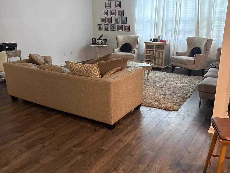 Spacious living room with wood-look floors, a comfortable seating setup, and large windows with curtain panels.