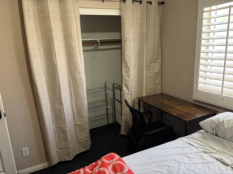 Bedroom includes a work desk, window with plantation shutters, and an open closet area with shelving for easy storage.