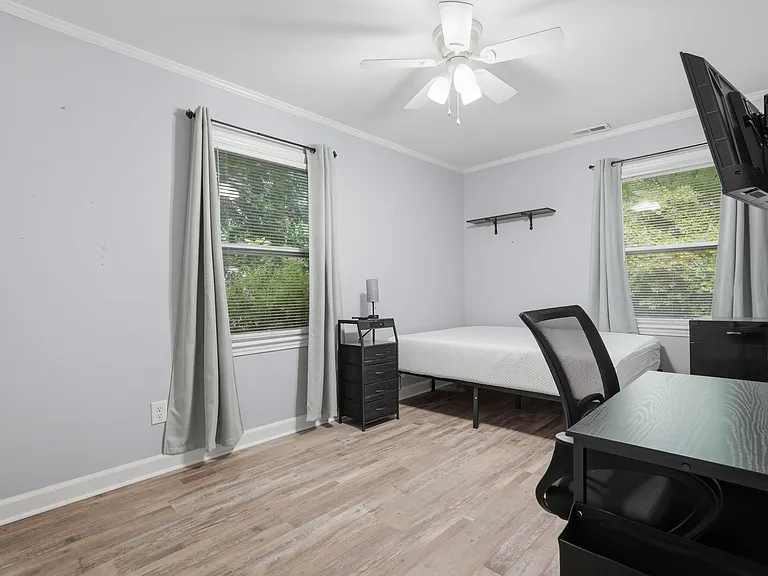 Furnished bedroom with two windows, ceiling fan, and durable wood-look flooring, plus a desk setup and wall shelf.