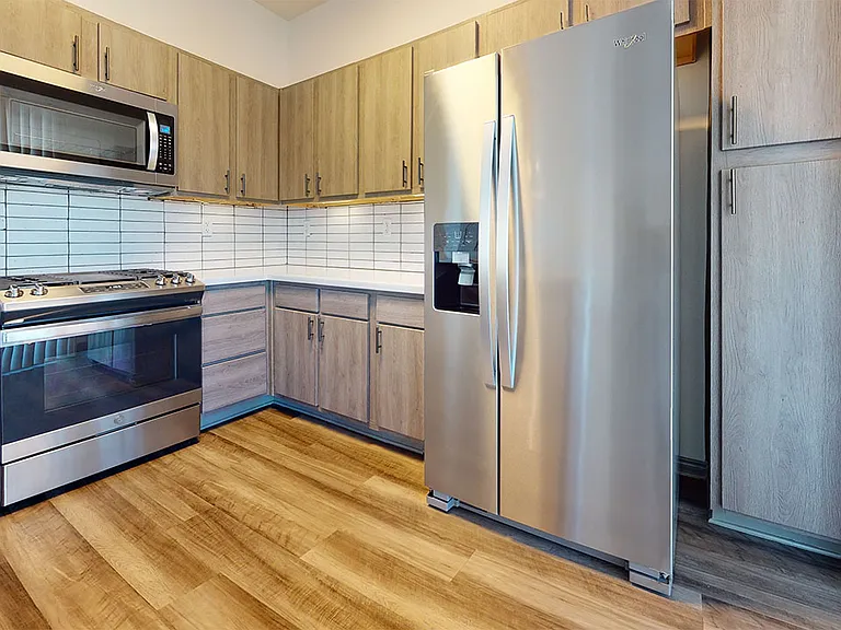 Apartment kitchen with stainless steel appliances, quartz countertops and wood-style flooring.