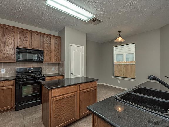 Island kitchen complete with gas stove, microwave, double sink, granite countertops, lots of cabinets for storage and tile floor.