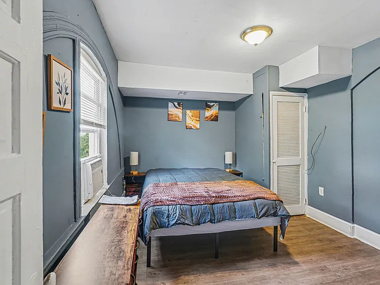 Furnished bedroom with a full-size bed, nightstands, and a window A/C unit, plus a louvered closet for storage.