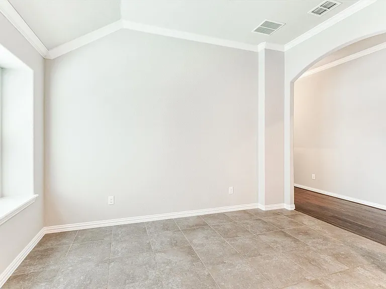 Spacious interior room featuring light-toned tile flooring, vaulted ceilings, and crown molding
