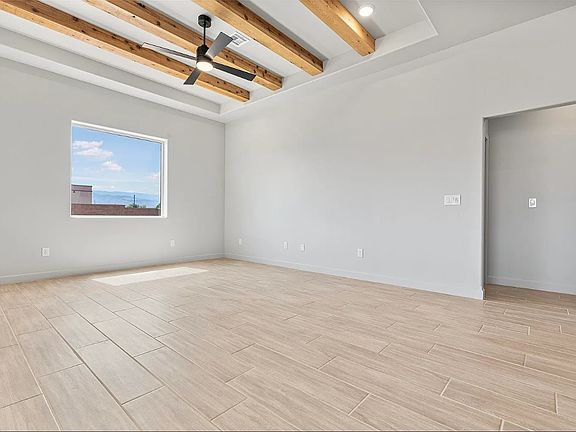 Bright, empty room with light wood tile flooring, white walls, a window, exposed wooden ceiling beam