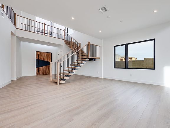 A spacious and modern interior with a wooden staircase, hardwood floors, and a large window overlook