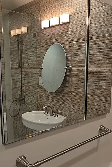 View of the Glass Medicine Cabinet with reflection of the Vanity Mirror, Sink & Lights