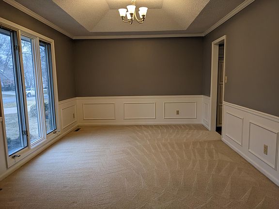 Versatile formal dining room or flex space with wainscoting, tray ceiling, and large front window.