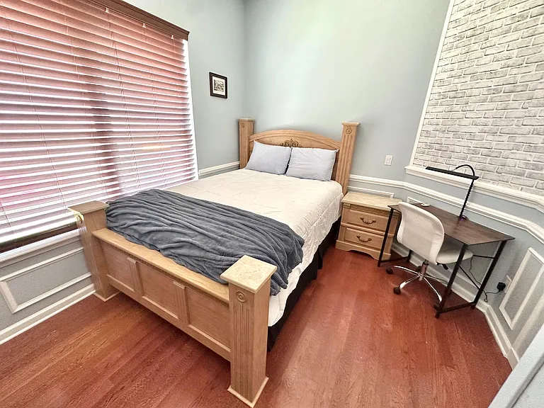 Hardwood floors, nightstand, and dedicated desk space beside a large window.