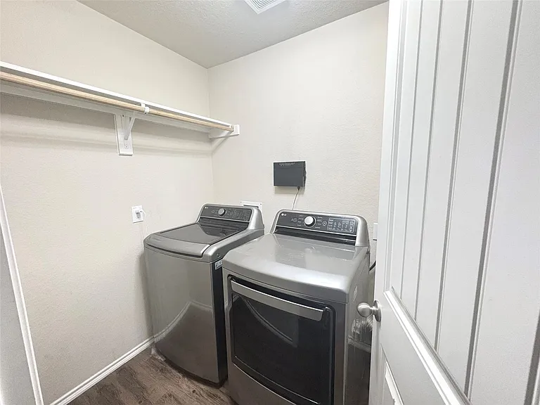 Dedicated laundry area featuring wood-finish flooring, light-toned walls, and a white overhead shelving and hanging rod system
