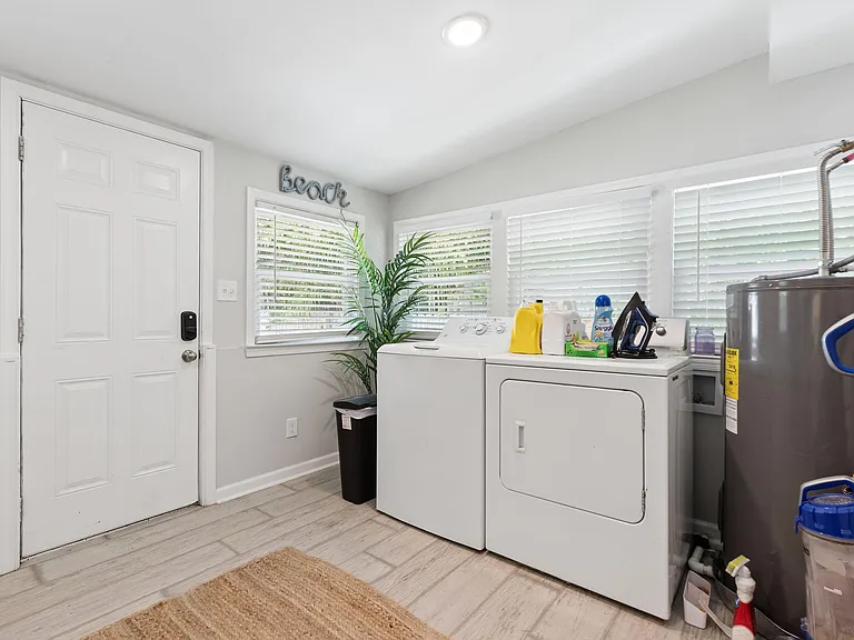Dedicated laundry area with side-by-side washer/dryer, wide windows with blinds, and durable tile flooring near entry.