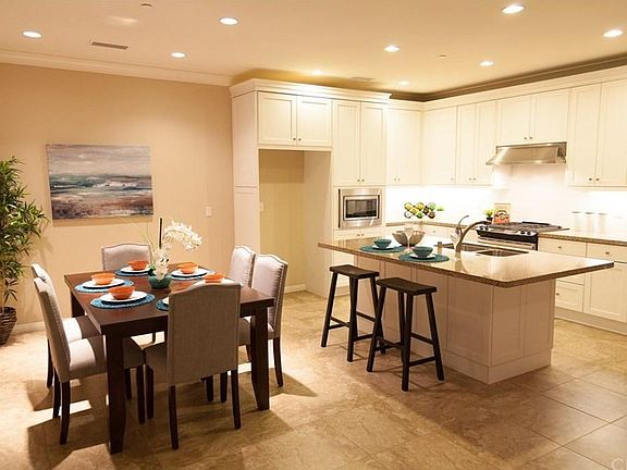 Large kitchen island with breakfast bar, granite countertops with subway tile backsplash, stainless steel appliances, white soft-close cabinetry, and recessed lighting throughout.