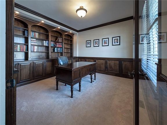 The luminous private home office is highlighted with custom built-in cabinetry, wainscoting, crown molding and a stained French 