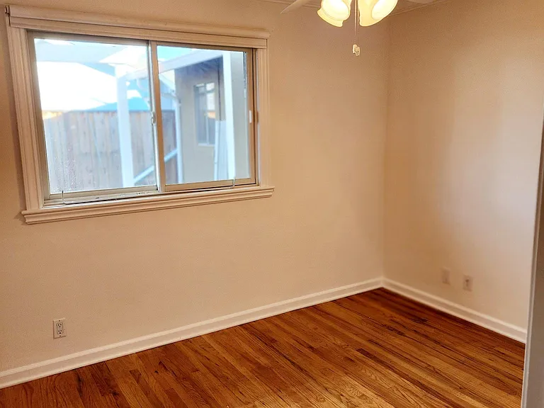 Bedroom #2 with hardwood floors, ceiling fan and window to backyard.