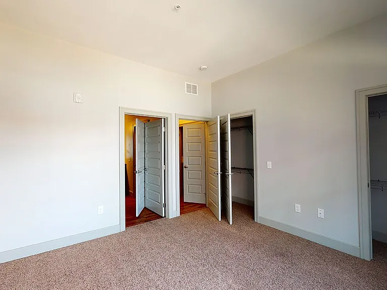 Spacious apartment bedroom with attached bathroom and plush carpet flooring.