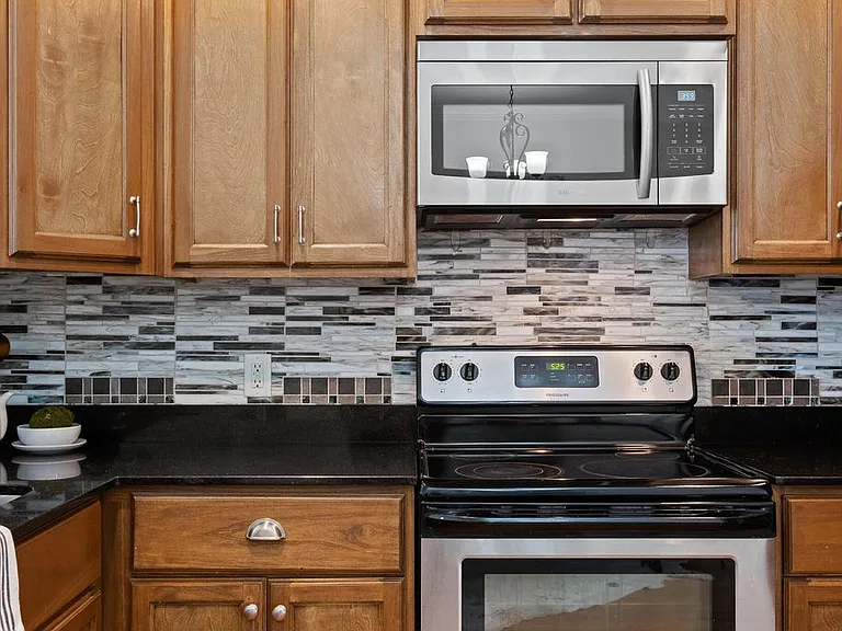 Granite counter tops and glass tile backsplash with microwave above stove top.