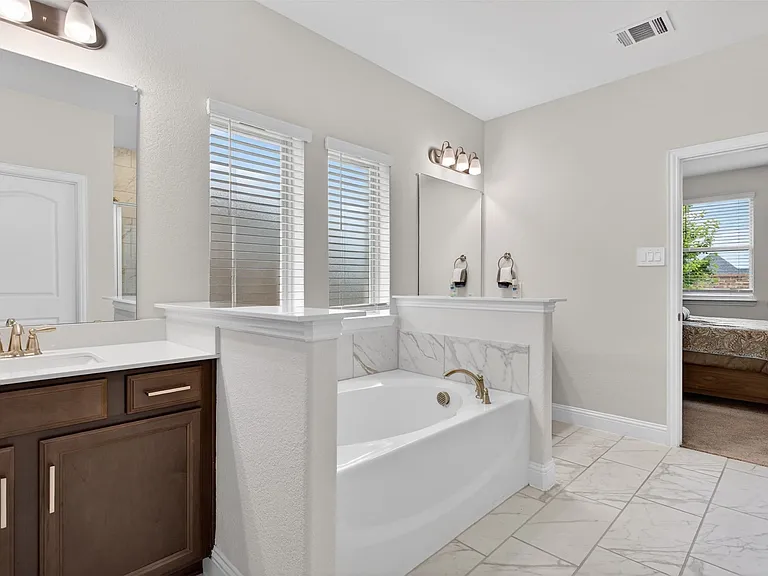 Bathroom featuring a soaking tub with a tiled surround, a single vanity with a quartz countertop, wood-finish cabinetry, and tiled flooring