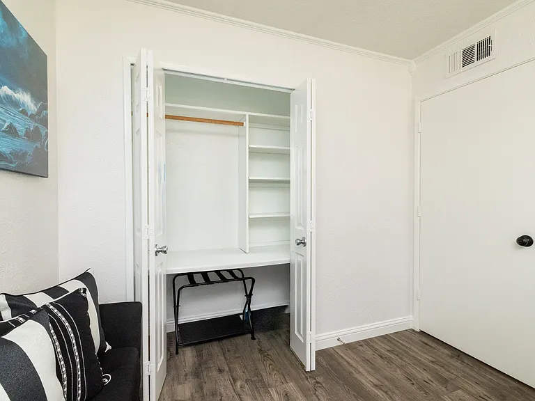 Bedroom 3 boasts a queen sized bed, cozy wood bed frame and headboard, a flat-screen Roku TV, and a comfy love seat_creating a peaceful and inviting space to relax and unwind. There is an attached closet with hangers and a luggage rack.
