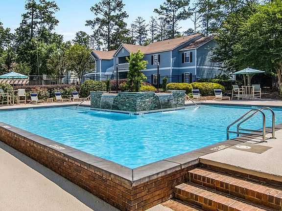 Outdoor pool with lounge chairs and umbrellas at Falls at Spring Creek apartments for rent in Macon, GA