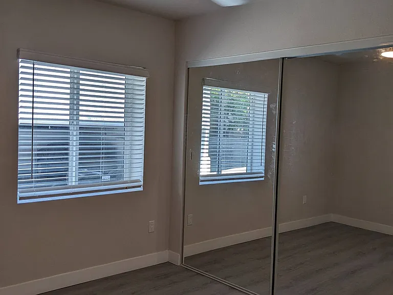 Bedroom with large window, mirrored closet doors, ceiling fan, and wood plank style flooring at The Hardison in Pasadena, California.
