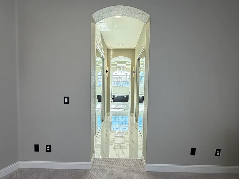 Hallway to primary suite bathroom with expansive mirrored closets on both sides leading to the primary bathroom