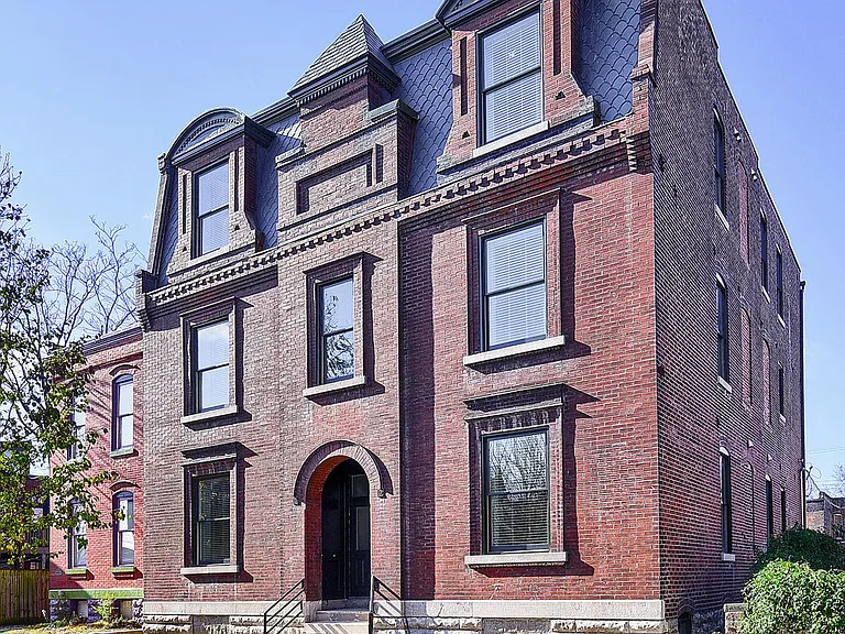Distinctive historic brick facade featuring ornate masonry, architectural detailing, teardrop slate mansard, and a welcoming arched entrance.
