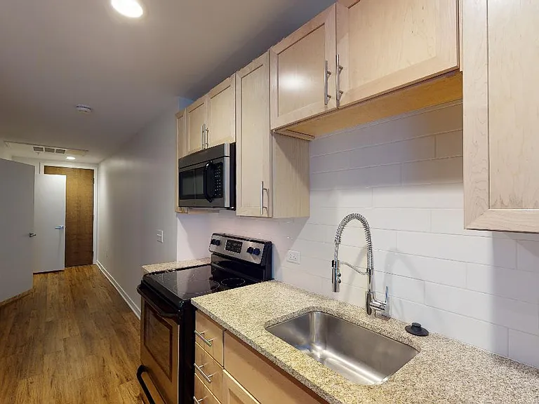 Apartment kitchen with stainless steel appliances, granite countertops and wood-style flooring.