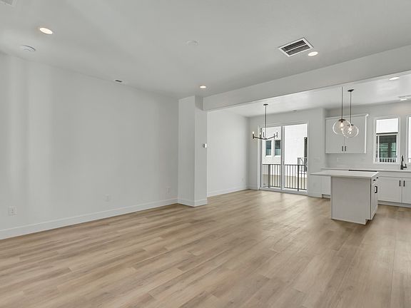An empty, modern kitchen and living area with light wood floors, white walls, recessed lighting, a l