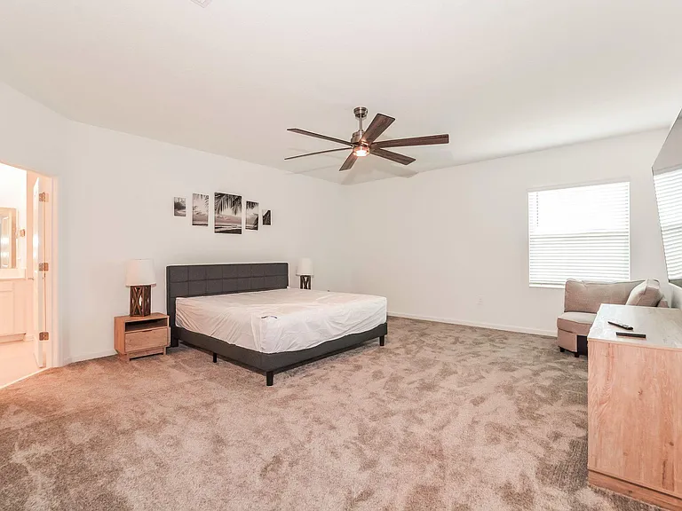 Spacious furnished bedroom with a ceiling fan, large window, and ensuite bath access, plus TV and seating area.