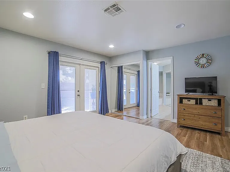 Primary suite showing french doors to the patio, bedroom closet, and door to the primary bathroom. Second closet with mirrored doors visible through the door.