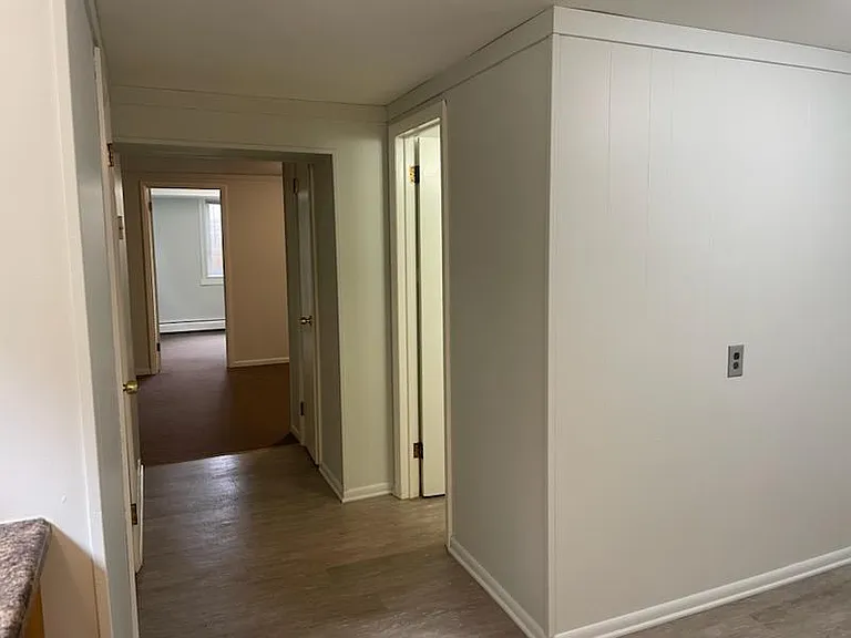 View of hall from kitchen into living room and bedroom. Door on right is bathroom.