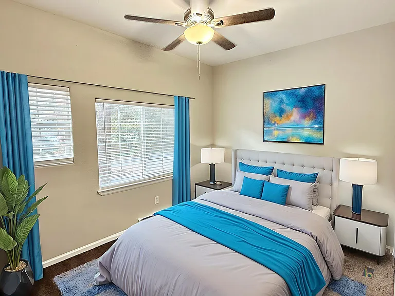Inviting bedroom with elegant decor, featuring a plush bed adorned with vibrant blue accents, modern artwork, and abundant natural light through wide windows.