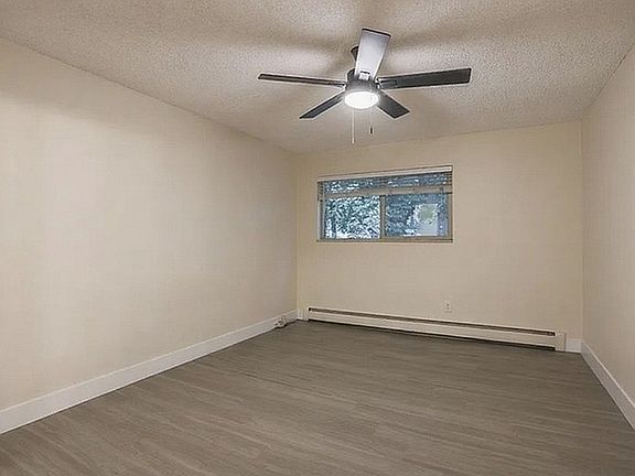 Inviting room with sleek wood flooring, modern ceiling fan, and large window providing natural light.