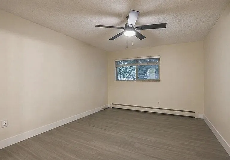 Inviting room with sleek wood flooring, modern ceiling fan, and large window providing natural light.
