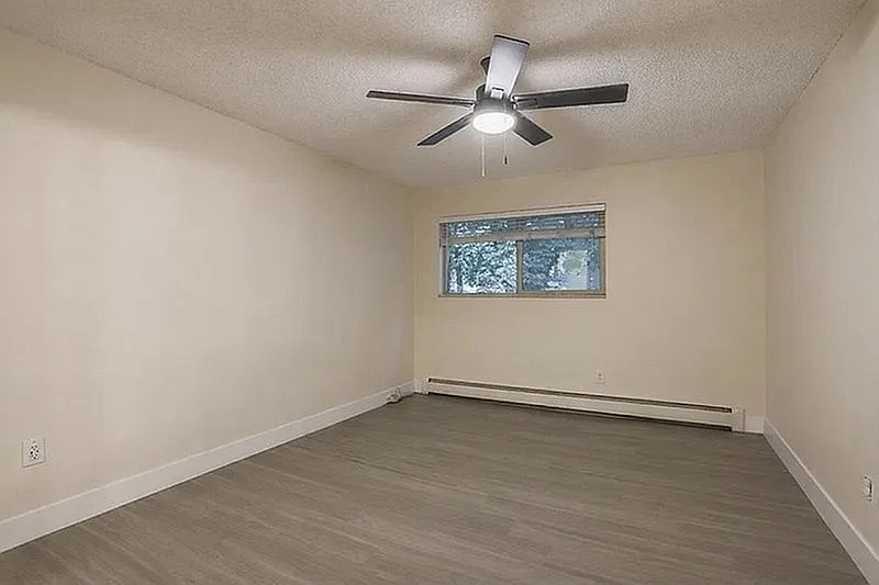 Inviting room with sleek wood flooring, modern ceiling fan, and large window providing natural light.
