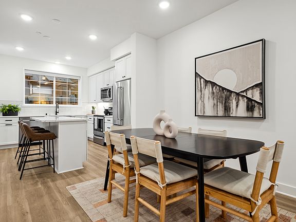 A modern and minimalist kitchen and dining area with a wooden dining table, chairs, and a large abst