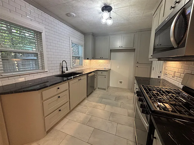 Kitchen featuring light gray cabinetry, dark countertops, a subway tile backsplash, stainless steel appliances, and tile flooring