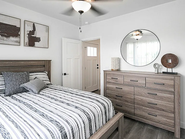 Chic bedroom with modern decor featuring a striped bedspread, wooden dresser, and round mirror, creating a cozy and stylish atmosphere.