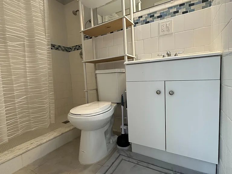 Full bathroom with tiled tub/shower combo, vanity with mirror, and built-in shelving for everyday storage.