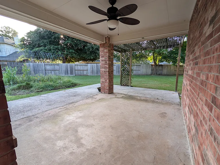 Relax on the spacious covered back patio equipped with an outdoor ceiling fan, extended open concrete extension, and a view of the expansive green backyard.