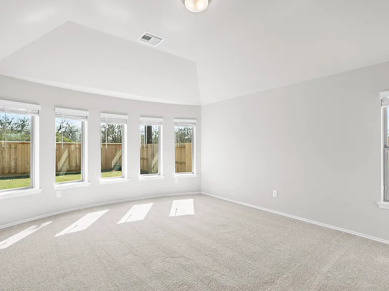 Sun-filled primary bedroom with the signature bow window featuring five large Low-E windows, vaulted ceiling, and plush carpet throughout.