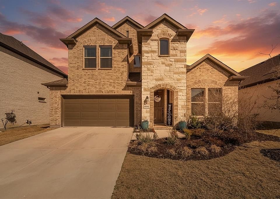 Two-story residence featuring a brick and stone facade, arched entry, attached two-car garage, concrete driveway, and landscaped front yard