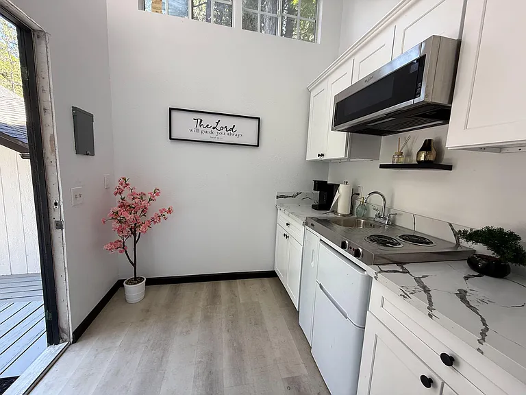 Compact kitchen with white cabinetry, marble-look counters, cooktop, microwave, and a sink with open shelving.