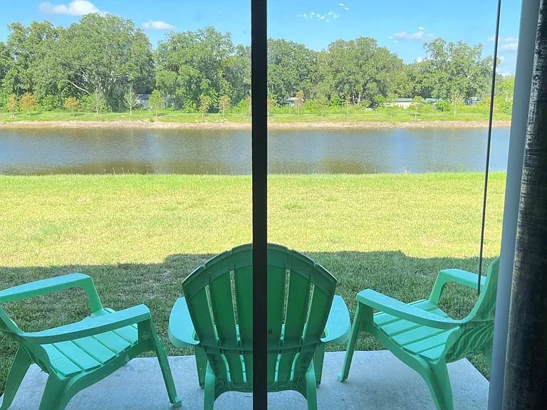 Covered patio seating overlooks a grassy yard and tranquil pond, offering a relaxing outdoor spot with scenic views.